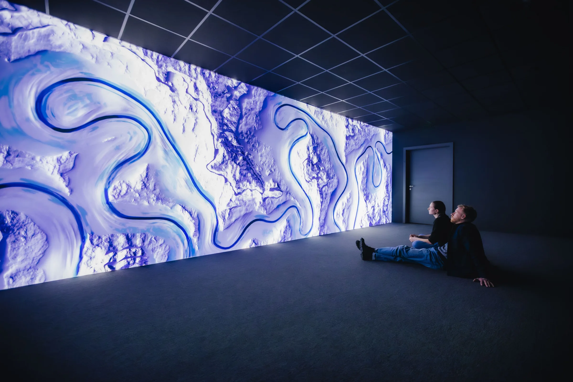 A visitor lying beneath the flowing blue projection wall of Signal UNIVERSE