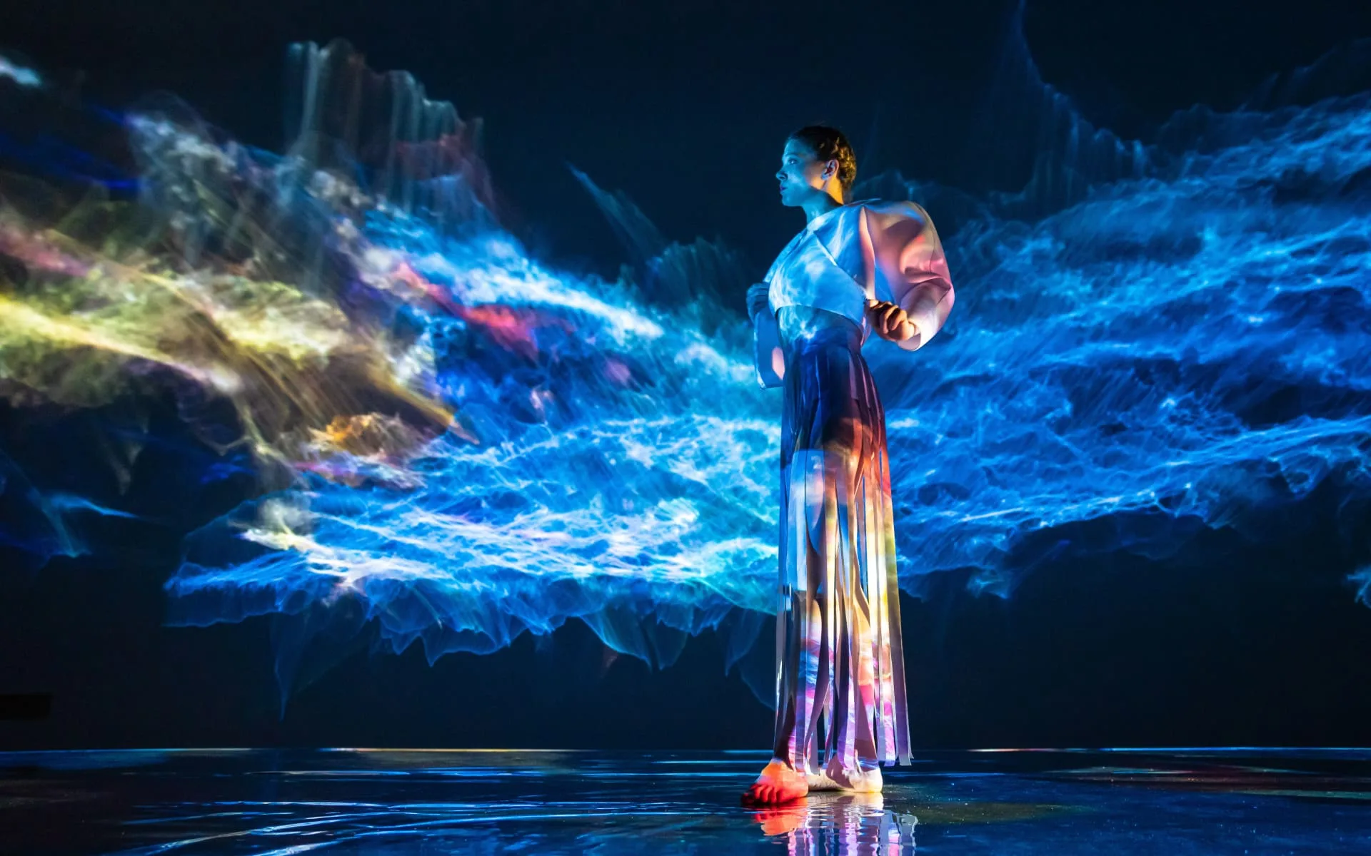 A visitor standing inside a room of moving light projections